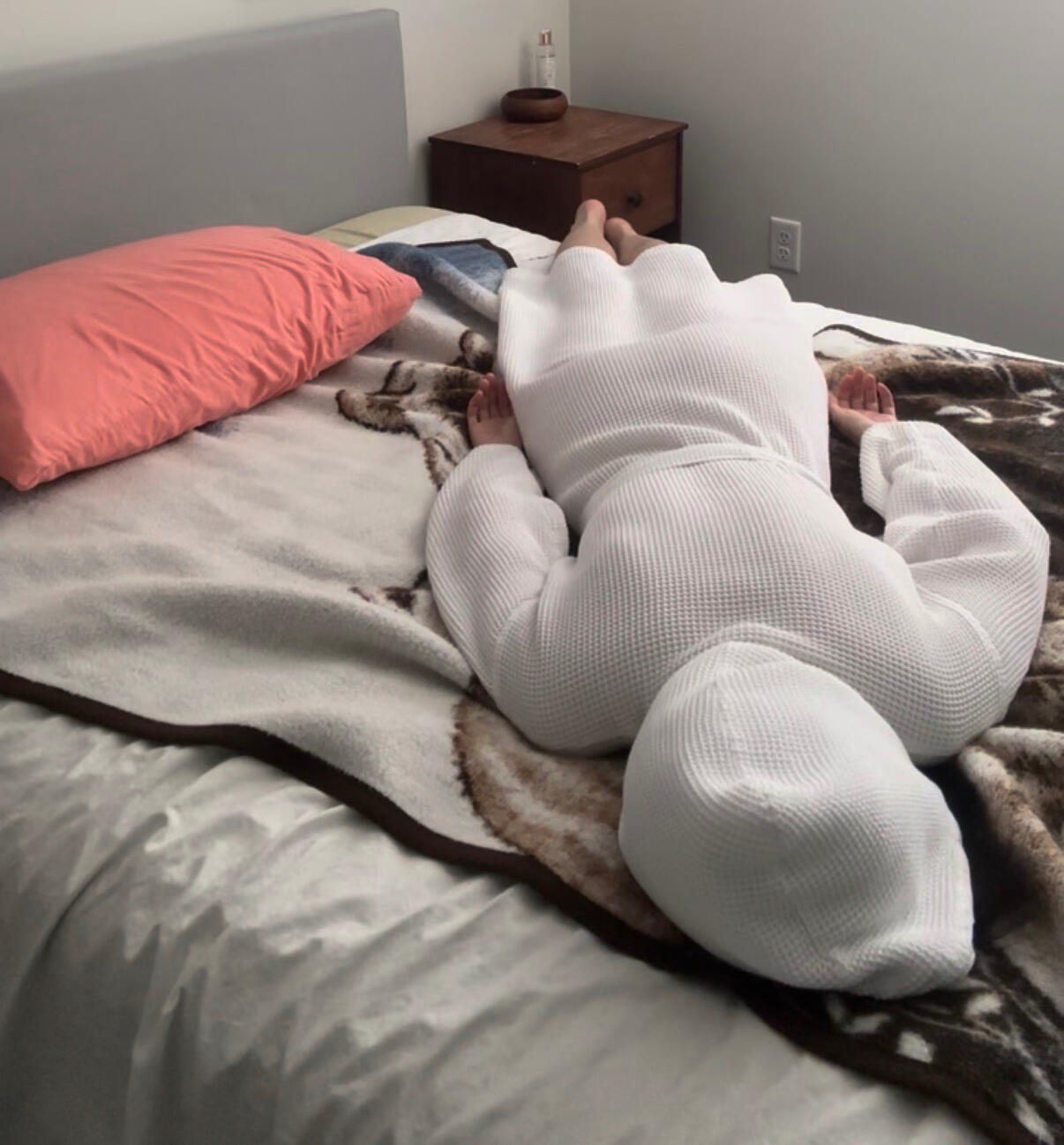 Autistic burnout by Layla Messner An exhausted woman lies face down on a bed, on top of a fuzzy blanket, wearing a white bathrobe.